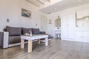 A modern living room with a grey sofa, a wooden coffee table with a vase, and a kitchen area with white cabinets and a tiled backsplash.