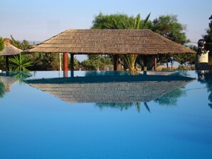 A swimming pool with a thatched-roof structure in the background.