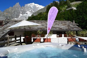 A hot tub with a mountain backdrop, a flag, and a wooden deck. - Pilier d'Angle (Courmayeur)