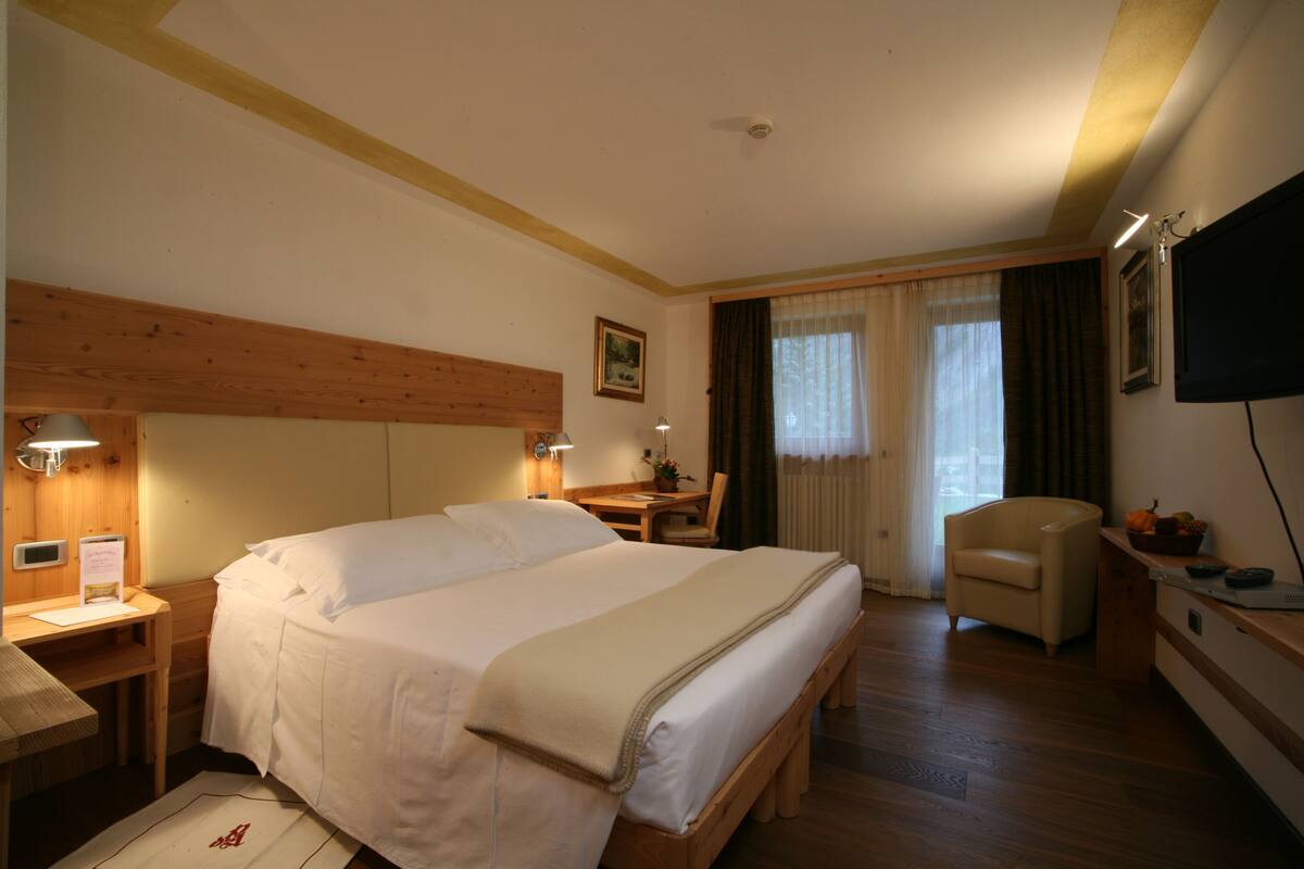 A hotel room with a large bed, a desk, a chair, and a television.