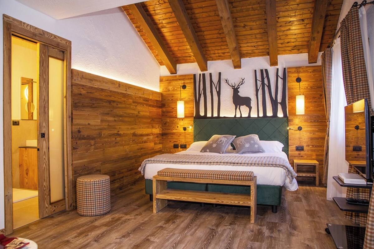 A wooden-paneled bedroom with a bed, bench, and wall-mounted lights.