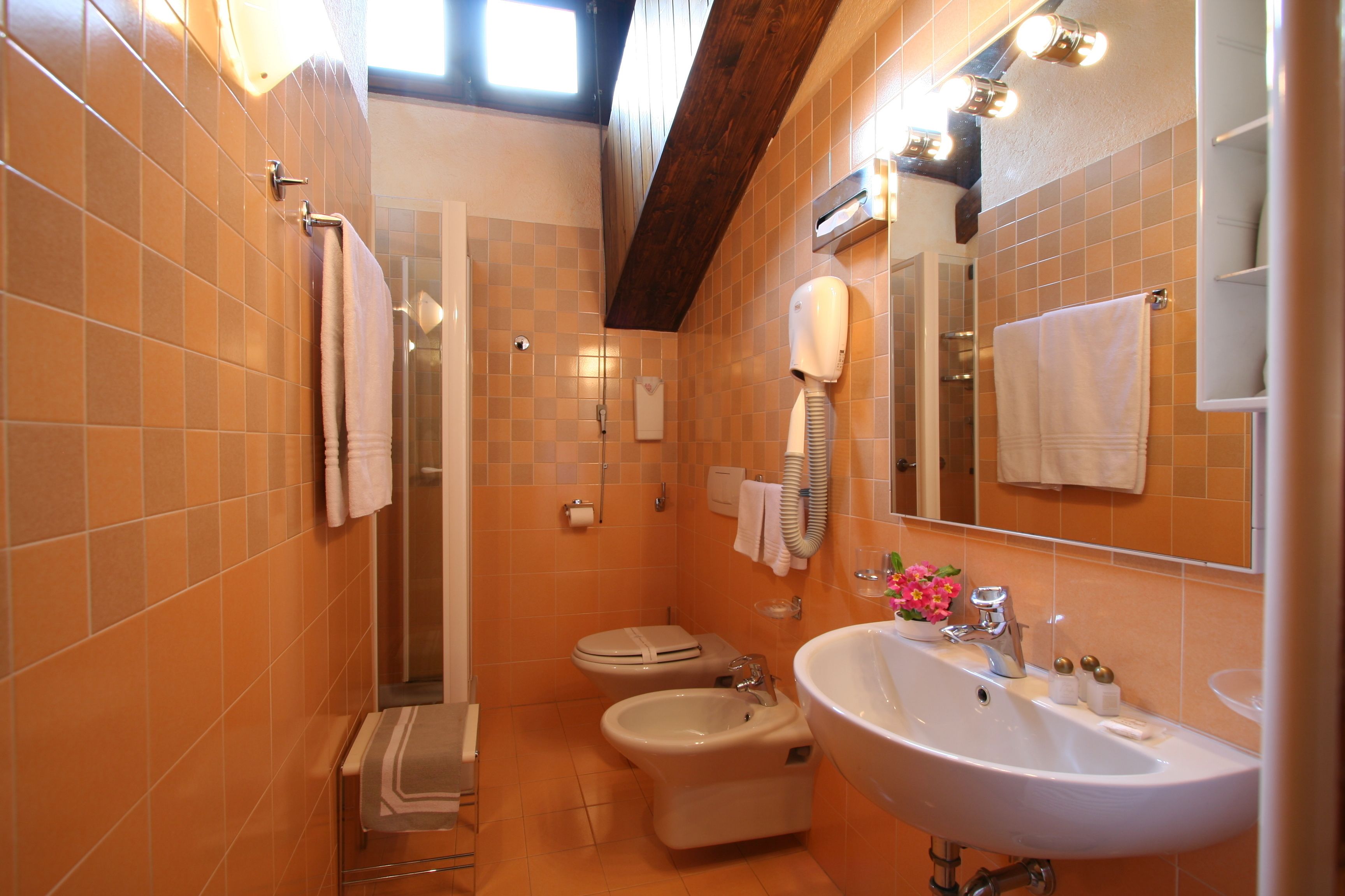 A bathroom with orange tiles, a sink, a bidet, and a toilet.