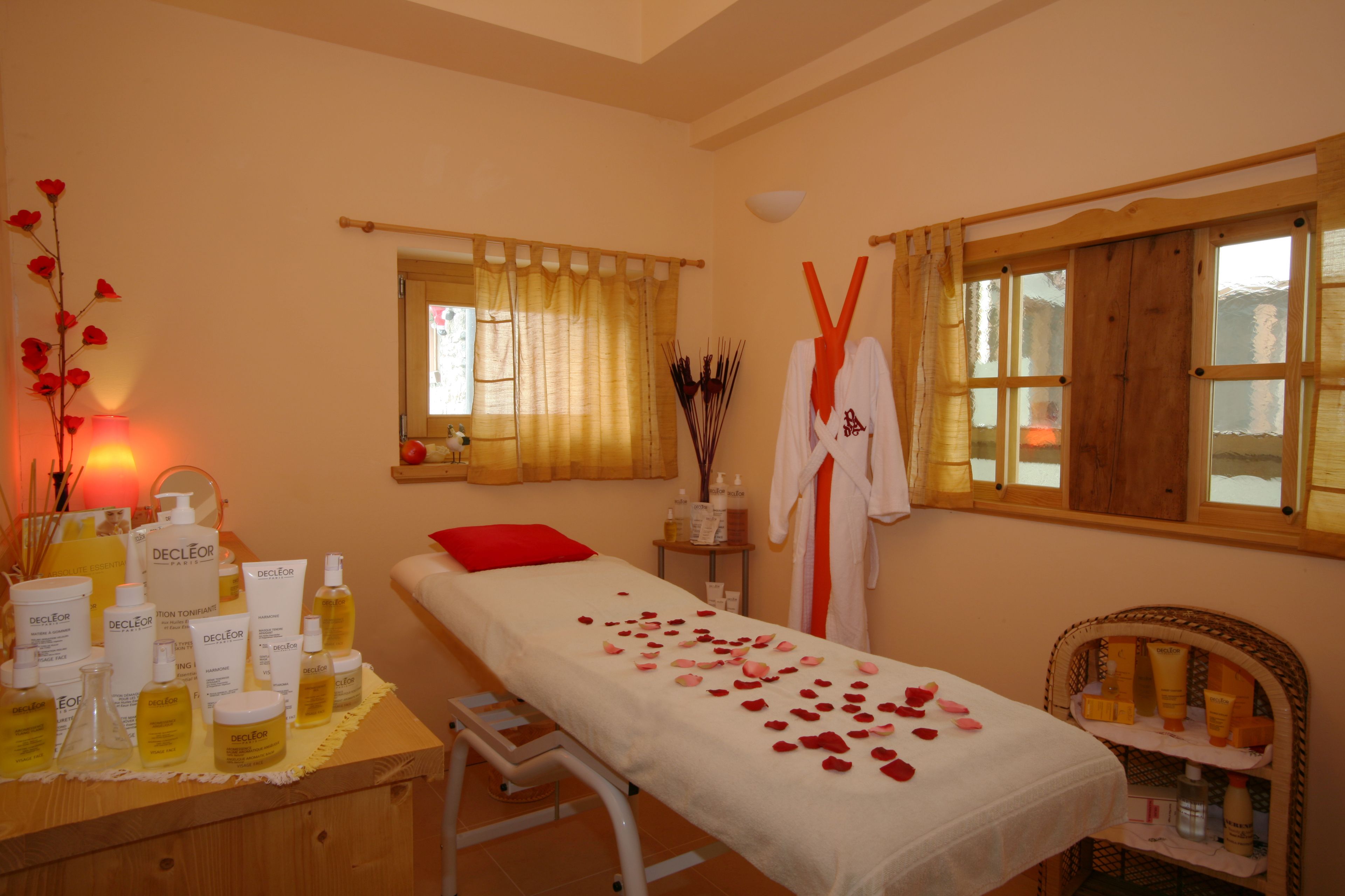 A spa room with a massage table, rose petals, and various skincare products on a table.
