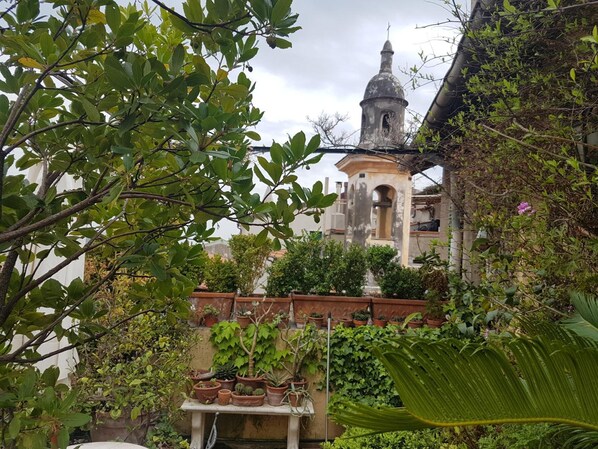 Une cour intérieure agrémentée de plantes en pot, une petite table et, au fond, un clocher.
