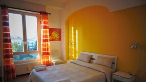 A bedroom with a large bed, a nightstand, a lamp, a window with curtains, and a radiator. - Bed and Breakfast Kemonia (Palermo)