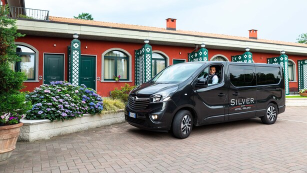 Una camioneta negra estacionada frente a un edificio rojo con puertas y ventanas verdes, identificado como "SILVER HOTEL MILANO".