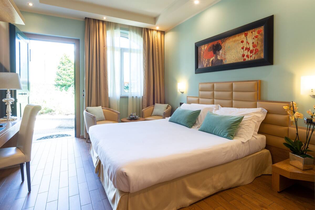 A hotel room with a large bed, two chairs, a desk, and a painting on the wall.