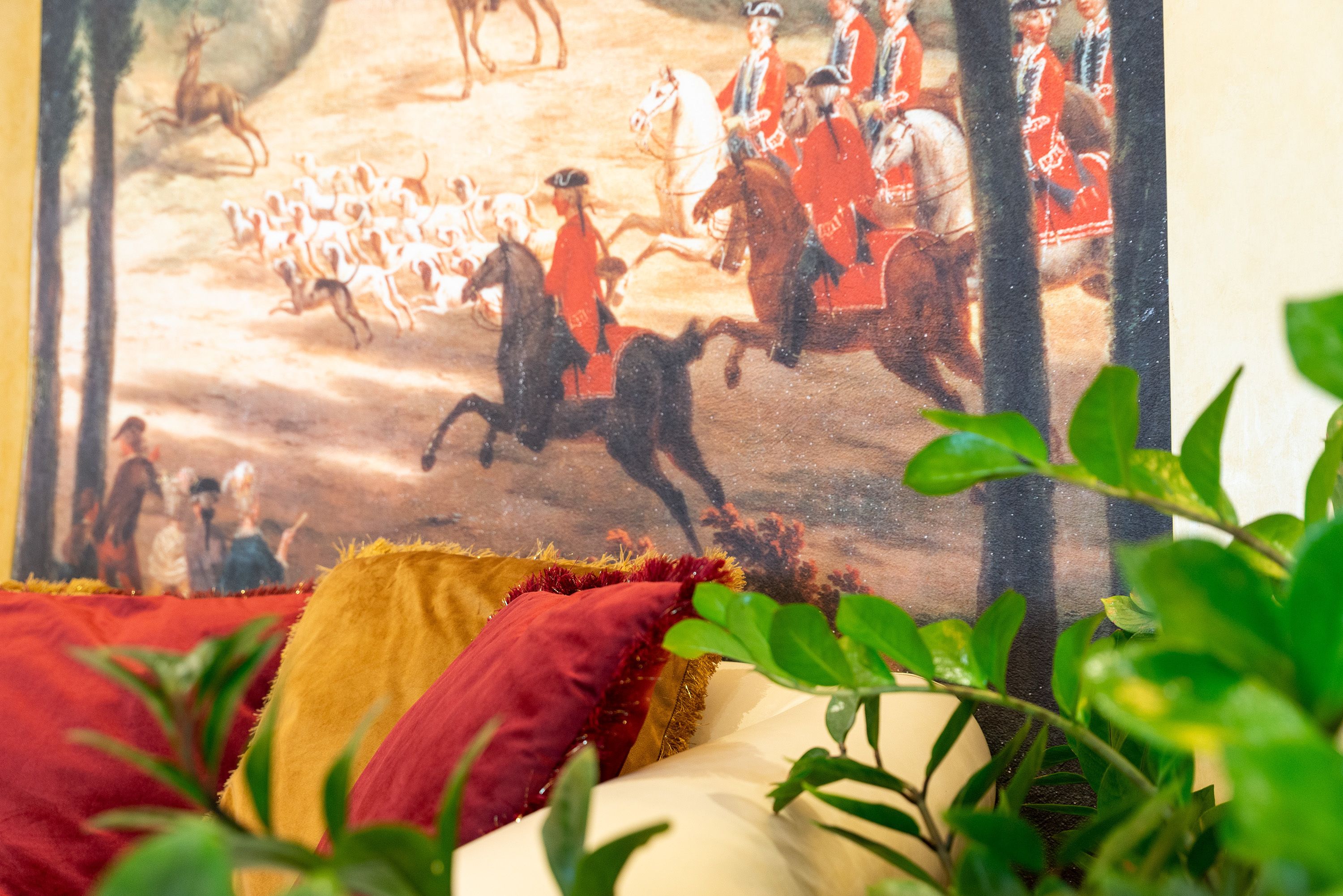 Pintura de una batalla histórica con soldados a caballo, parcialmente cubierta por una cama y plantas verdes.