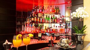 A bar area with multiple shelves of liquor bottles, two glasses of orange cocktails, and a decorative metal bowl on the counter. - Hotel Silver (Milan)