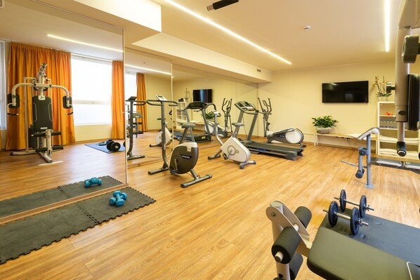 Een sportschool met trainingsapparatuur, een spiegelwand en een televisie.