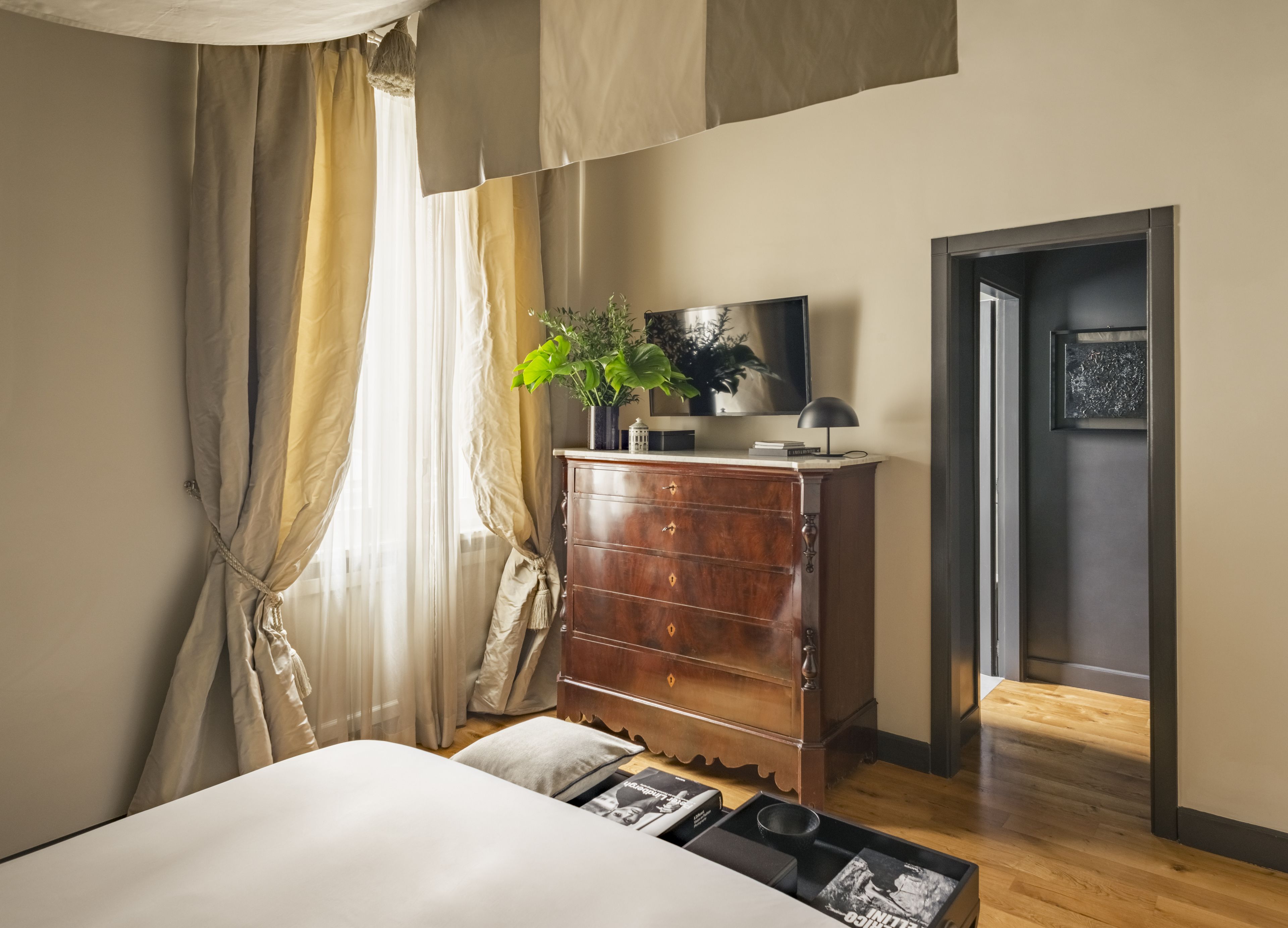 A bedroom with a bed, a wooden dresser, a potted plant, a television, and a framed picture on the wall.