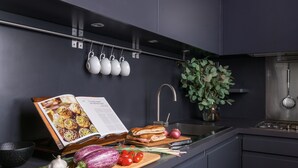 A modern kitchen with dark cabinetry, a hanging tea set, a cookbook, fresh vegetables, and a potted plant. - Crossing Condotti (Rome)
