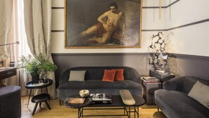 A modern living room with a dark grey sofa, a small round table, and a painting of a nude figure. - Crossing Condotti (Rome)