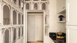 A hallway with ornate architectural details, a wooden floor, and a kitchen area with a black countertop and a coffee maker. - Crossing Condotti (Rome)