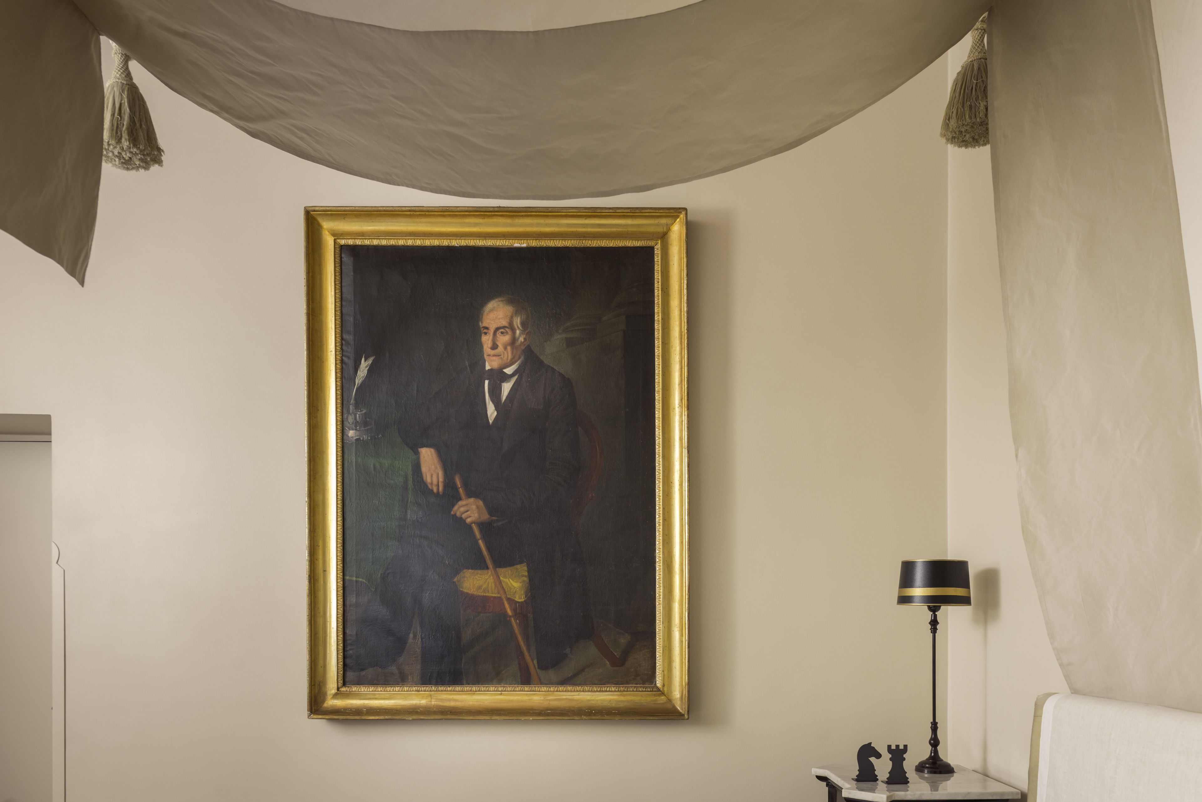 A portrait painting on a wall, a lamp on a side table, and a chair.