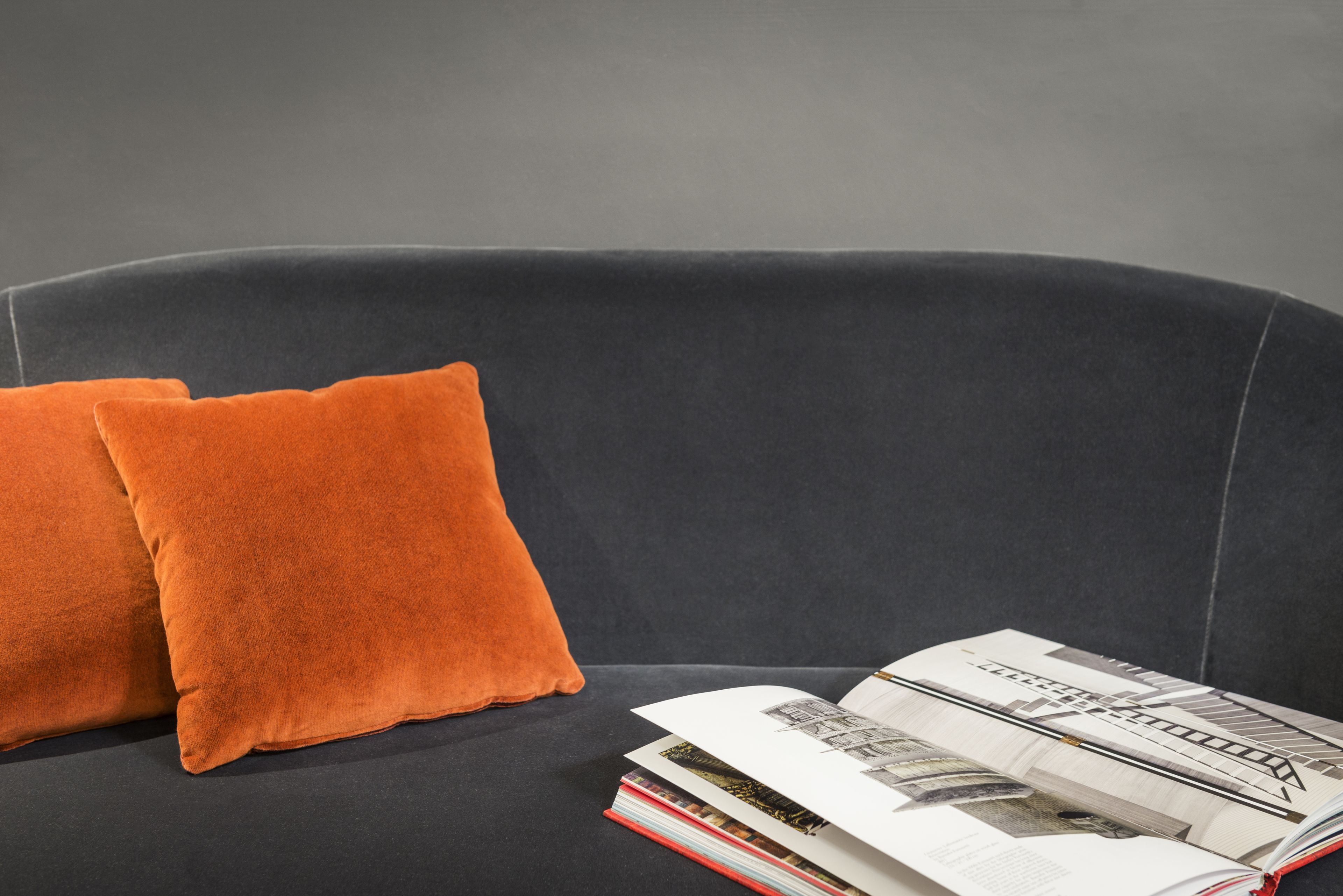 En mørkegrå sofa med to orange puder og et magasin på ryggen.