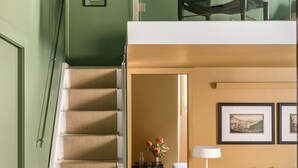 A staircase leading to a second-floor area with a bed, a floor lamp, and framed pictures on the wall. - Crossing Condotti (Rome)