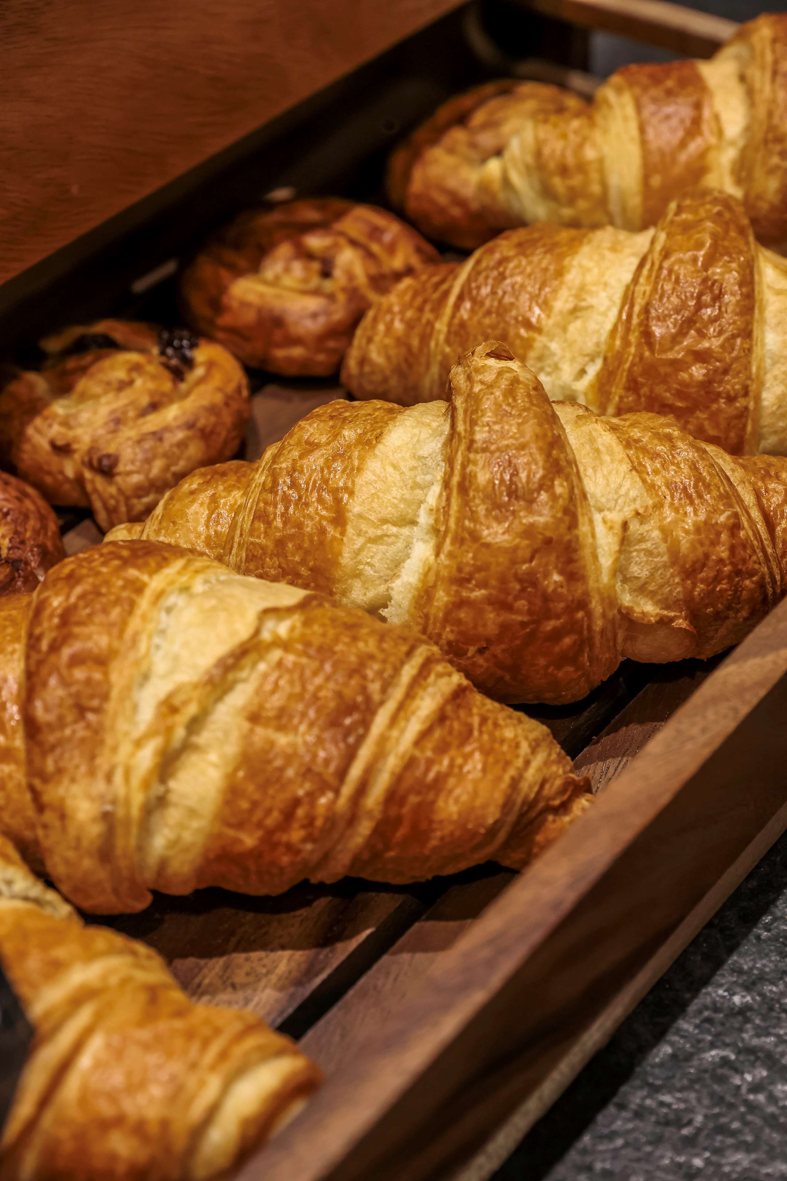 Una bandeja de diversos pasteles, incluyendo croissants y otras delicias horneadas, presentada en una bandeja de madera.