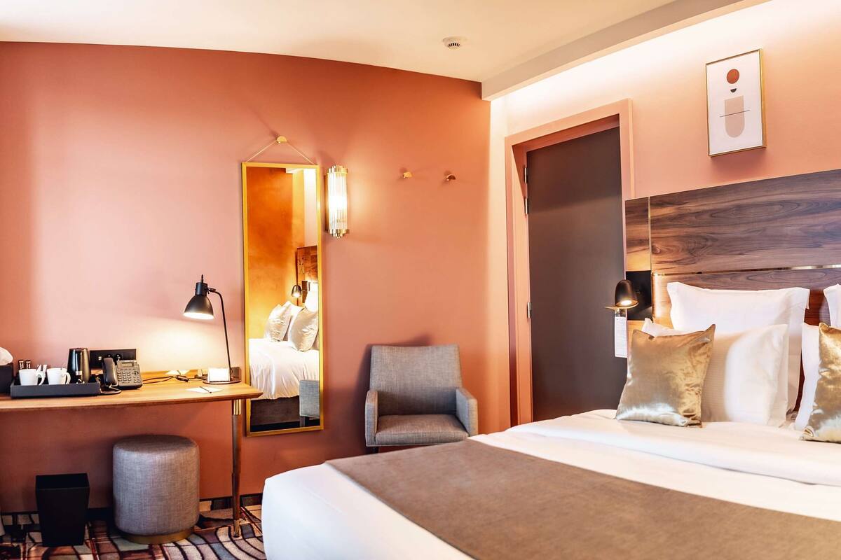 Une chambre d’hôtel avec un grand lit, un bureau avec une chaise, un miroir et un luminaire fixé au mur.