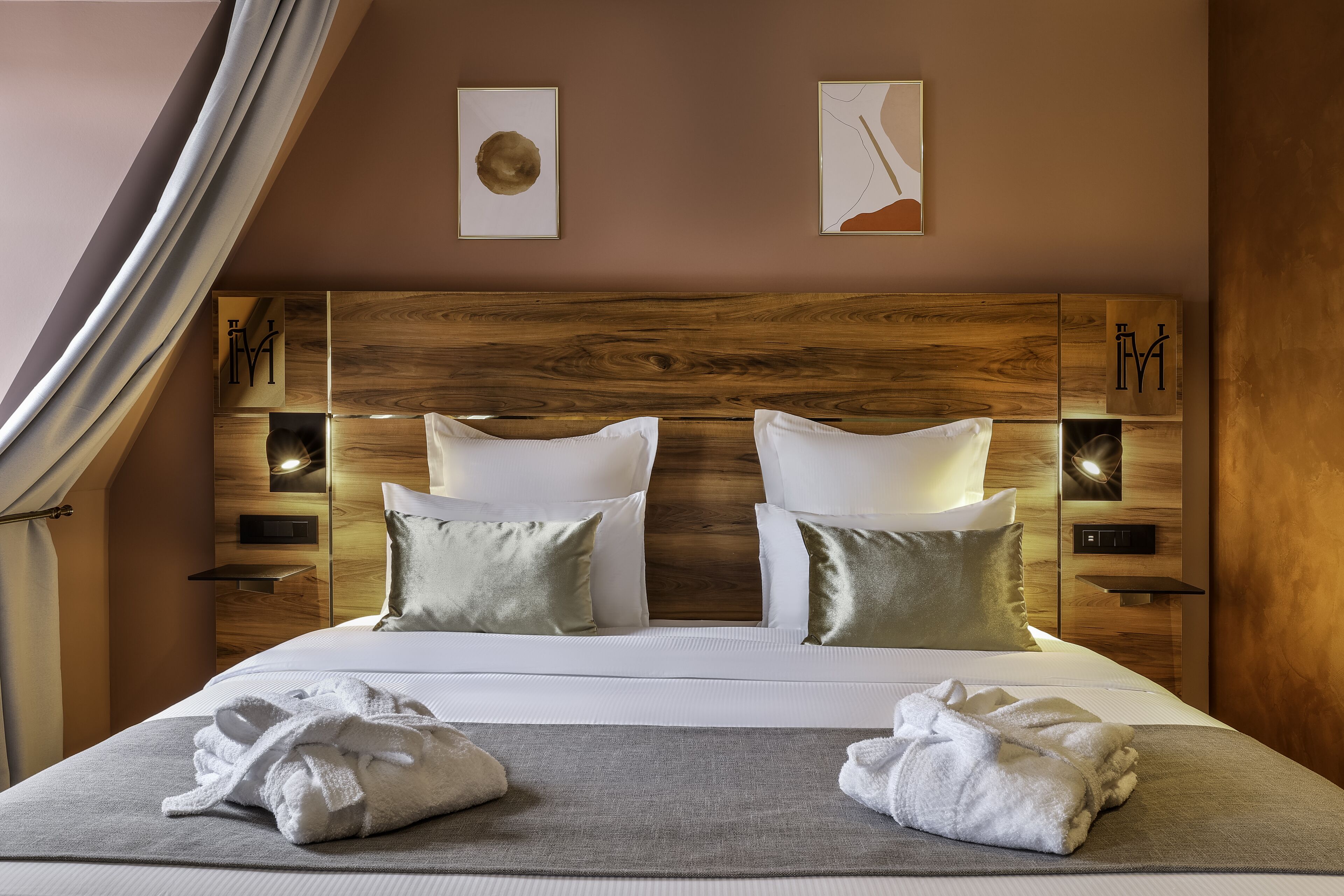 A neatly made bed with white linens and two pillows, a wooden headboard, and two wall-mounted nightstands with lamps.
