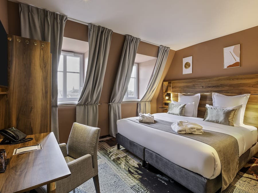 A hotel room with a bed, a desk, a chair, and a telephone.