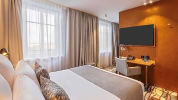 Ein Hotelzimmer mit einem großen Bett, einem Schreibtisch mit Stuhl, einem Flachbildfernseher und einem Fenster mit Vorhängen.