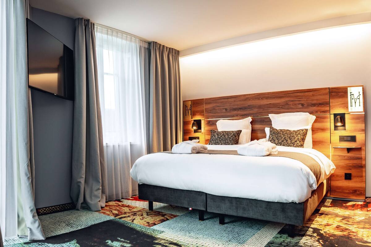 Une chambre d’hôtel moderne avec un grand lit, une tête de lit en bois et un téléviseur à écran plat fixé au mur.