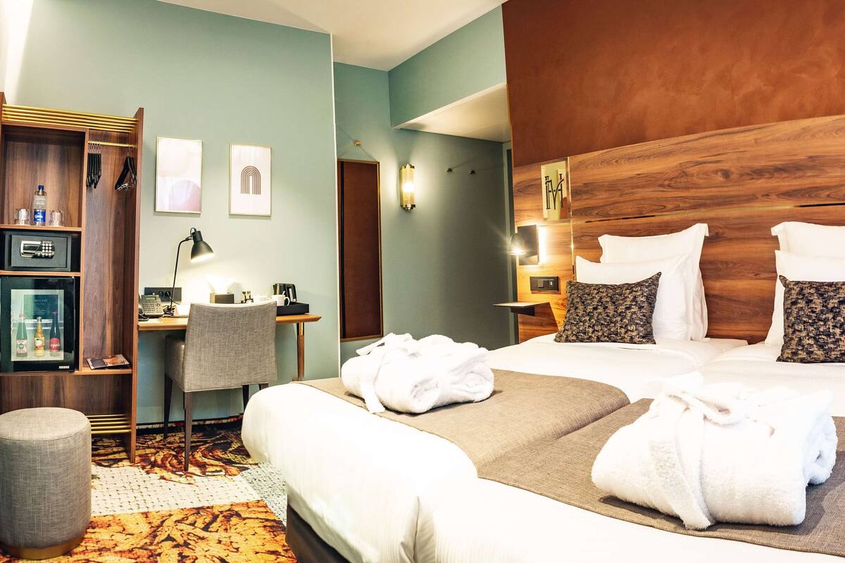 Une chambre d’hôtel équipée d’un lit, d’un bureau, d’une chaise, d’un mini-bar et d’un téléviseur fixé au mur.