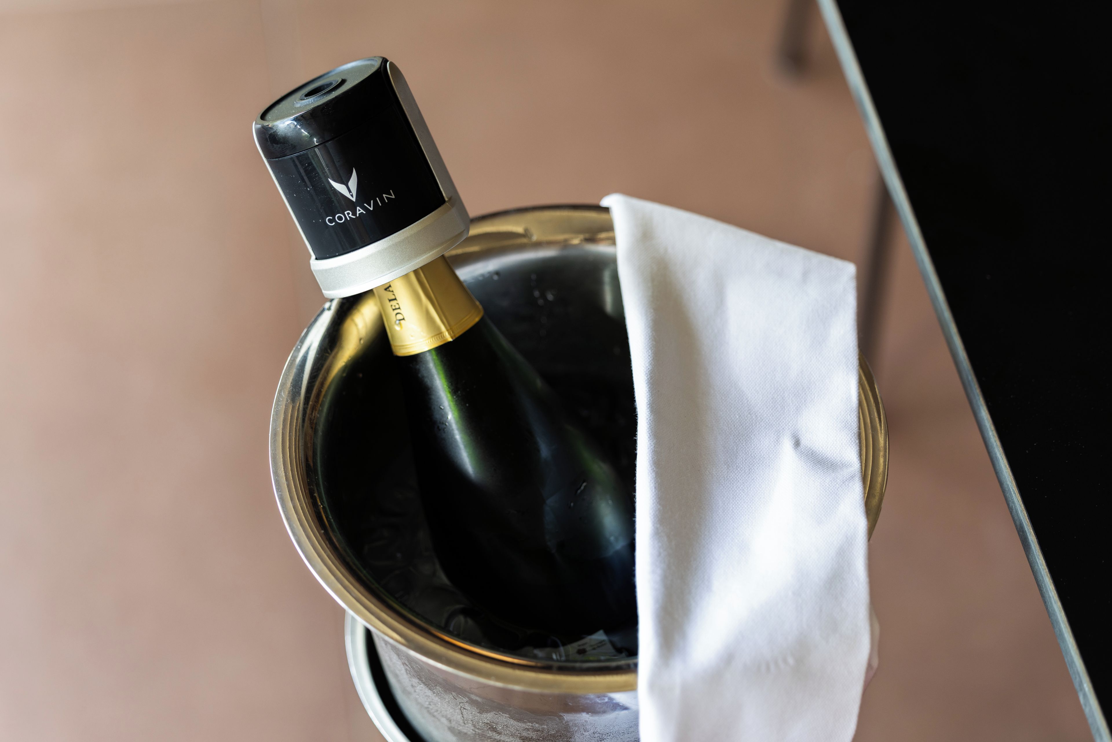 Una bottiglia di vino con etichetta nera e dorata, parzialmente avvolta in un panno bianco, posta in un contenitore metallico.