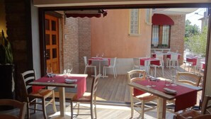 An outdoor dining area with tables and chairs, a brick wall, and a wooden deck. - Hotel Noce (Brescia)