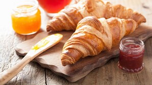 Two croissants on a wooden board with a knife and two jars of jam. - Hotel Noce (Brescia)