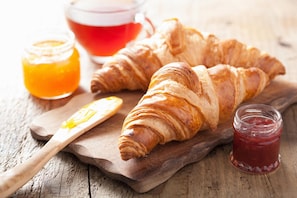 Two croissants on a wooden board with a knife and two jars of jam. - Hotel Noce (Brescia)