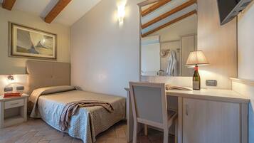 A bedroom with a bed, bedside table, lamp, desk, chair, and a mirror.
