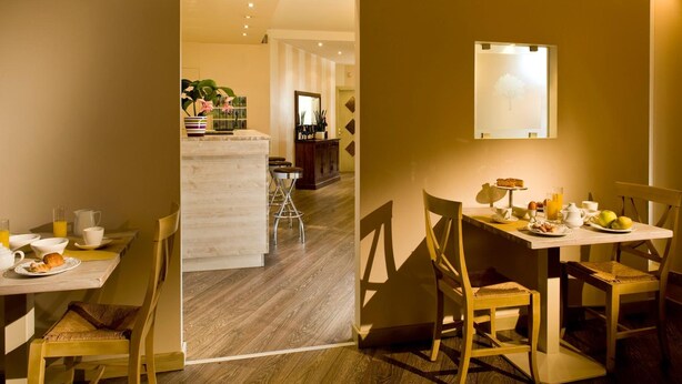 A hotel room with a wooden floor, a dining area with a table set for breakfast, and a small kitchen area in the background. - Hotel Noce (Brescia)