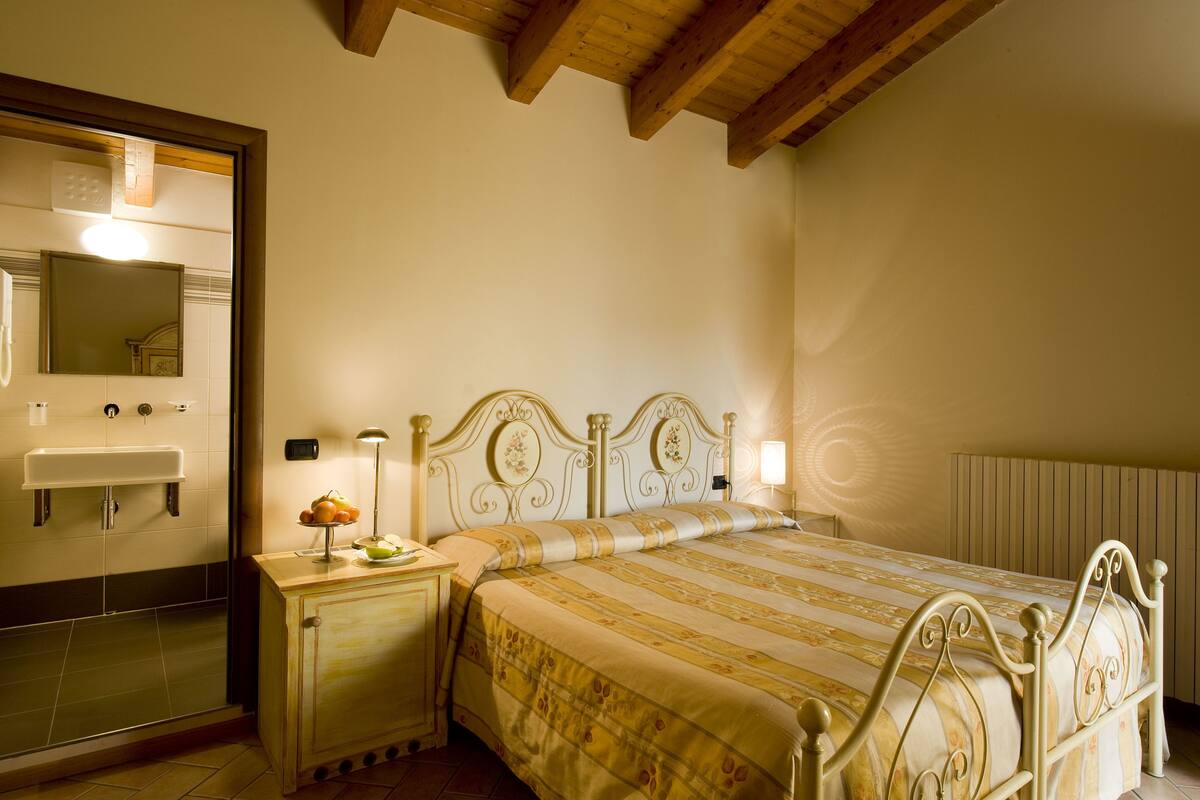 A bedroom with a bed, bedside table, lamp, and a mirror.