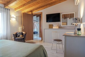Hotellihuone, jossa on sänky, työpöytä kannettavalla tietokoneella, tuoli, vaatekaappi ja seinälle asennettu televisio.