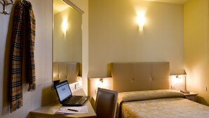 A hotel room with a bed, a desk with a laptop, a chair, a nightstand with a lamp, and a mirror. - Hotel Noce (Brescia)