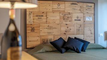 A bedroom with a wooden headboard displaying various wine labels, a bed with dark blue pillows, and a lamp on a bedside table.