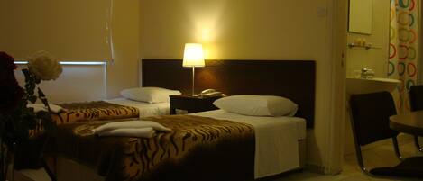 A hotel room with two beds, a nightstand with a lamp, a chair, and a bathroom visible in the background.