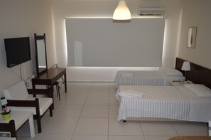 A hotel room with a bed, a desk, a chair, a TV, and a large window. - Lordos Hotel Apartments (Limassol)