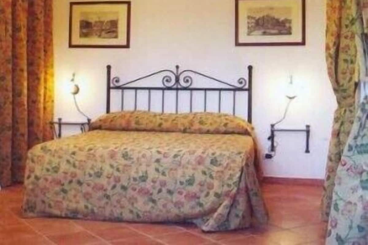 A bedroom with a bed, two wall-mounted lamps, and two framed pictures on the wall.