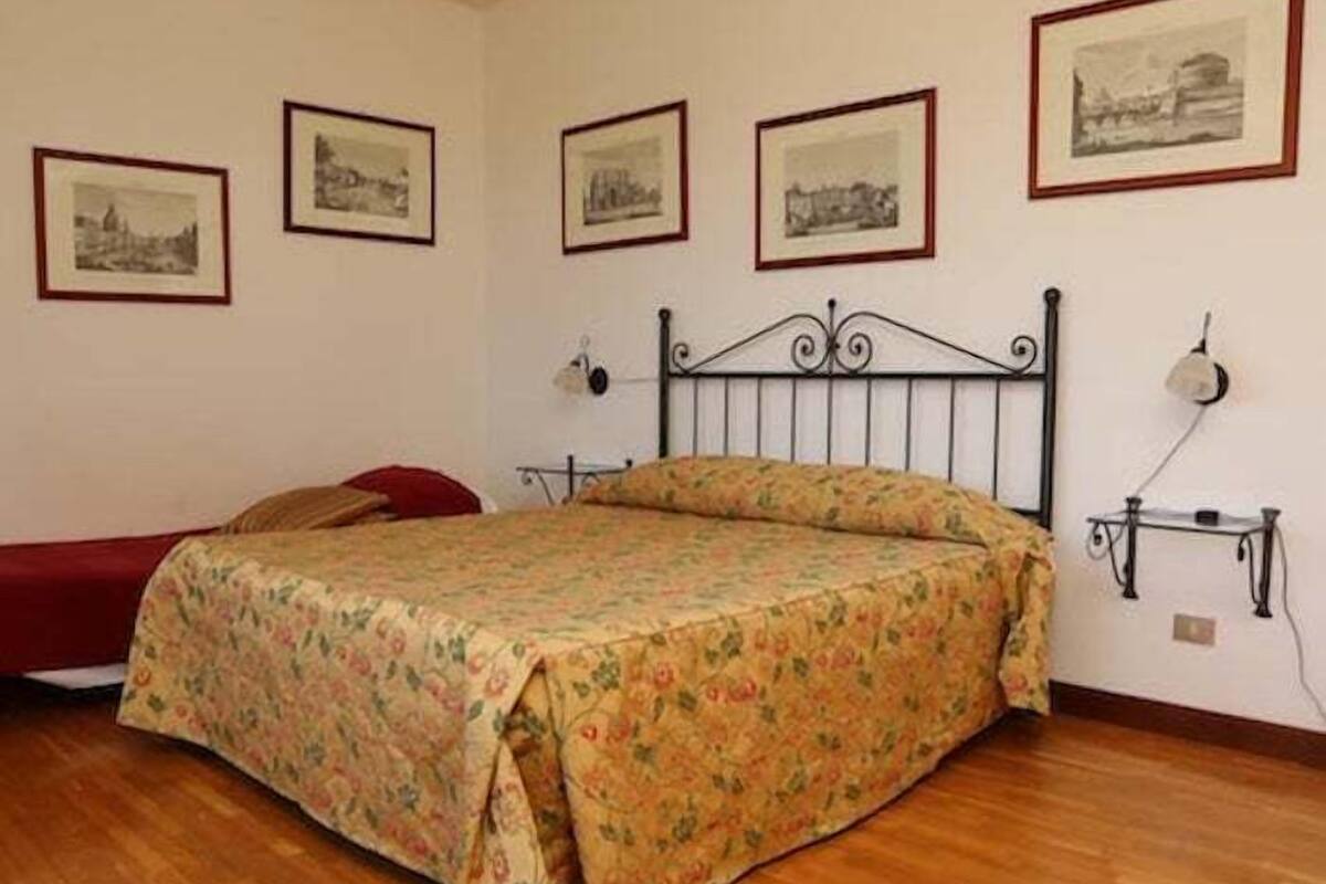 A bedroom with a bed, a bedside table, a lamp, and four framed pictures on the wall.