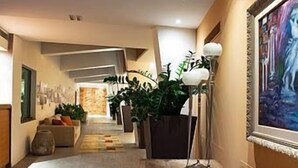 A hotel corridor with a sofa, potted plants, and artwork on the walls.