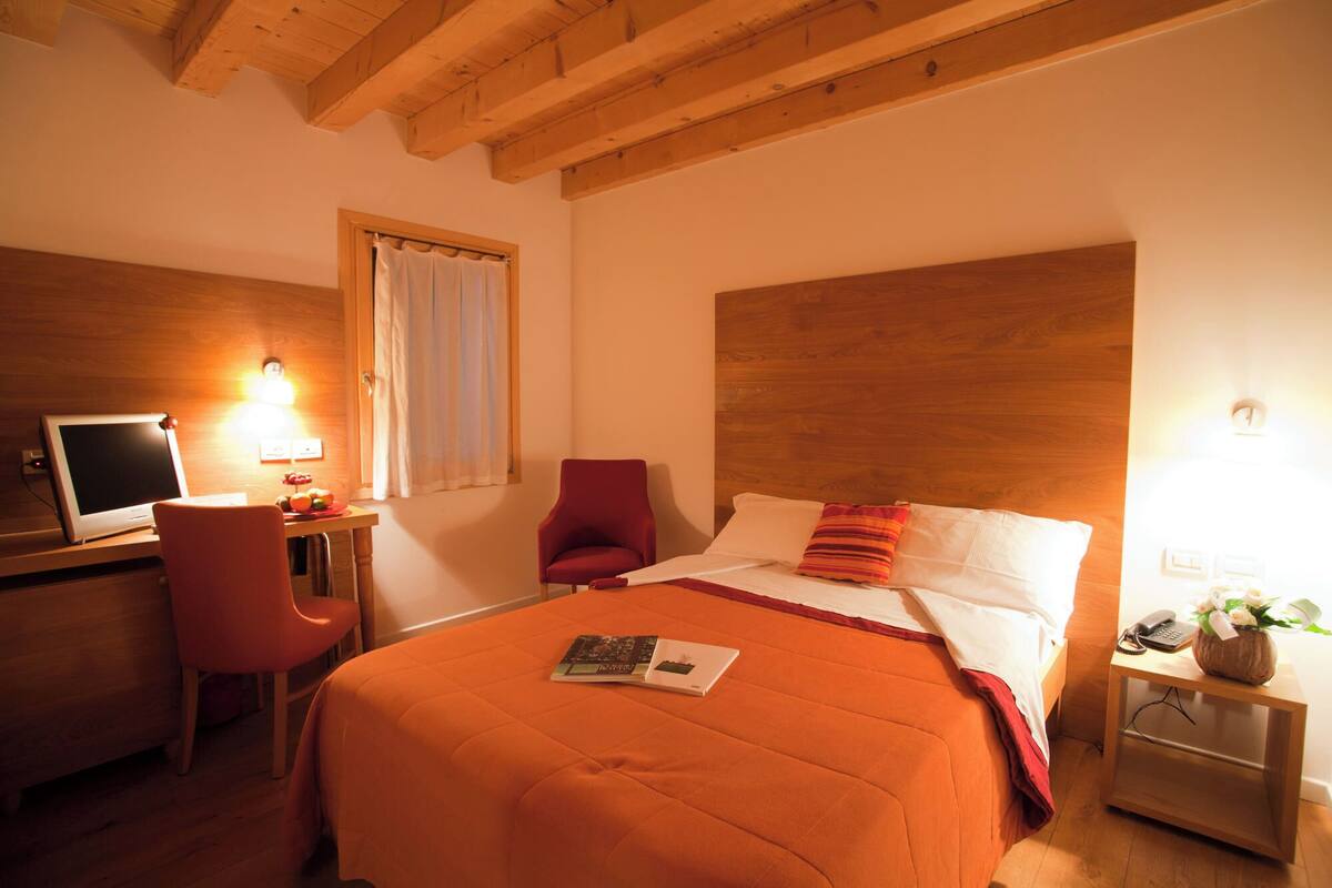 Une chambre d’hôtel avec un lit, un bureau équipé d’un ordinateur, une chaise et une table de chevet avec un téléphone et des fleurs.