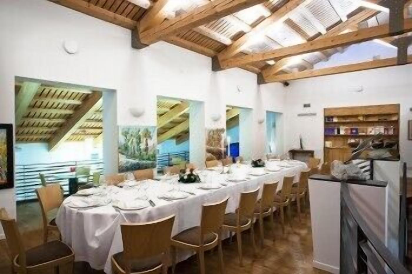Comedor con una larga mesa dispuesta para una comida, vigas de madera en el techo y una estantería con diversos objetos.