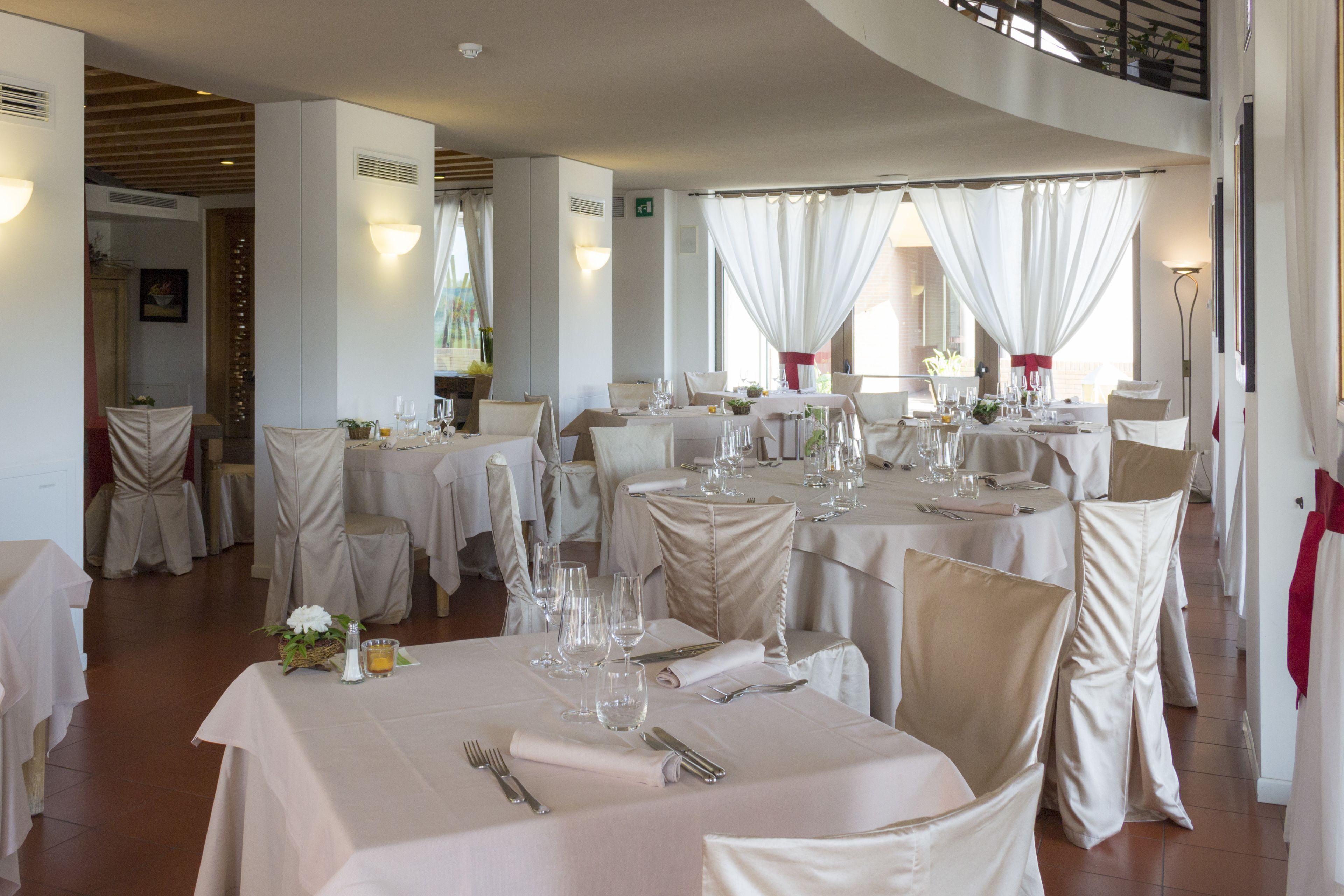 A restaurant with round tables, white tablecloths, and beige chairs.