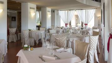 A restaurant with round tables, white tablecloths, and beige chairs.