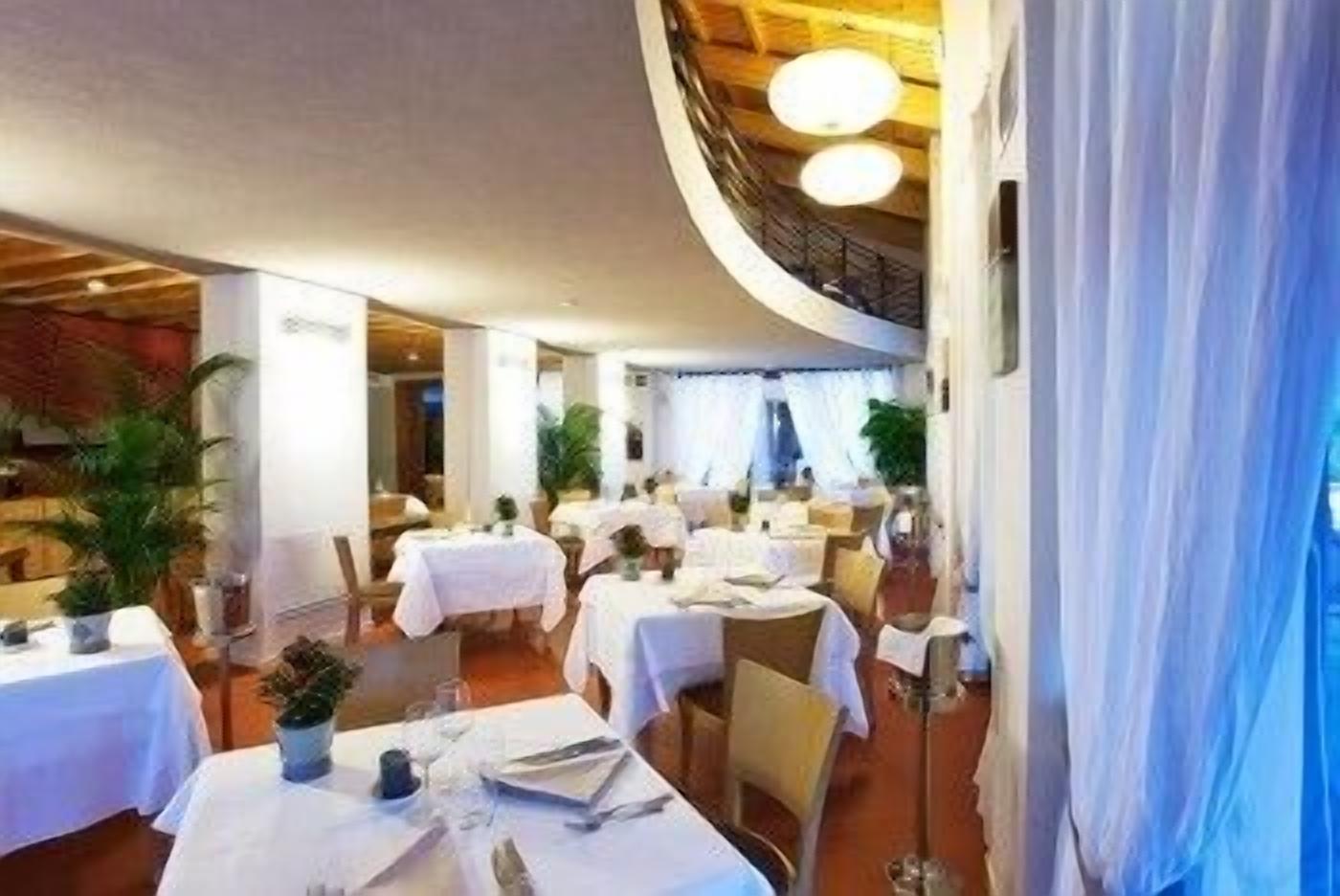 Un restaurante con mesas redondas, manteles blancos y plantas en macetas.