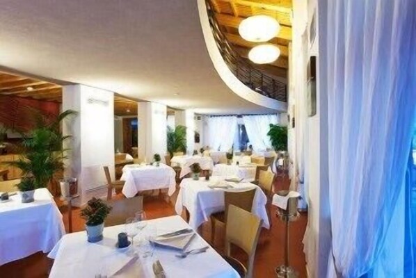 Un restaurante con mesas redondas, manteles blancos y plantas en macetas.