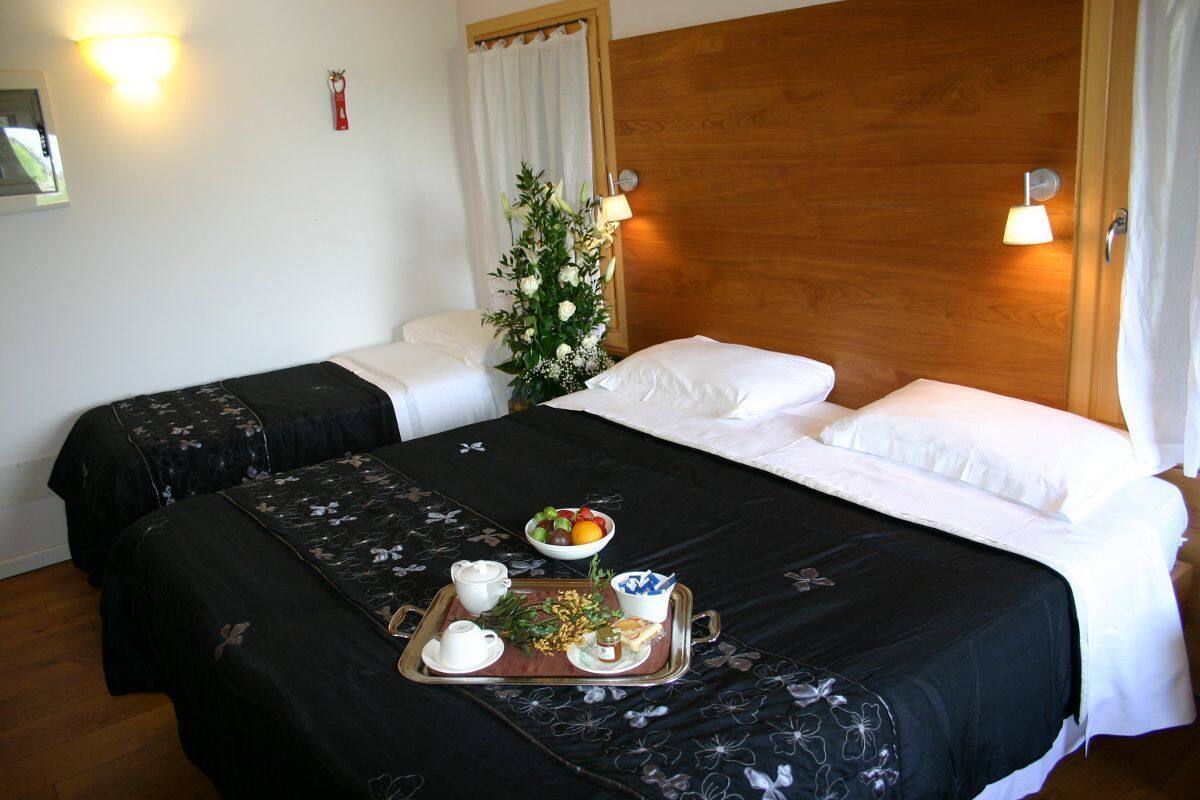 Une chambre d’hôtel avec deux lits, une tête de lit en bois, une couvre-lit à motifs floraux, un plateau avec des articles pour le petit-déjeuner et une plante décorative.